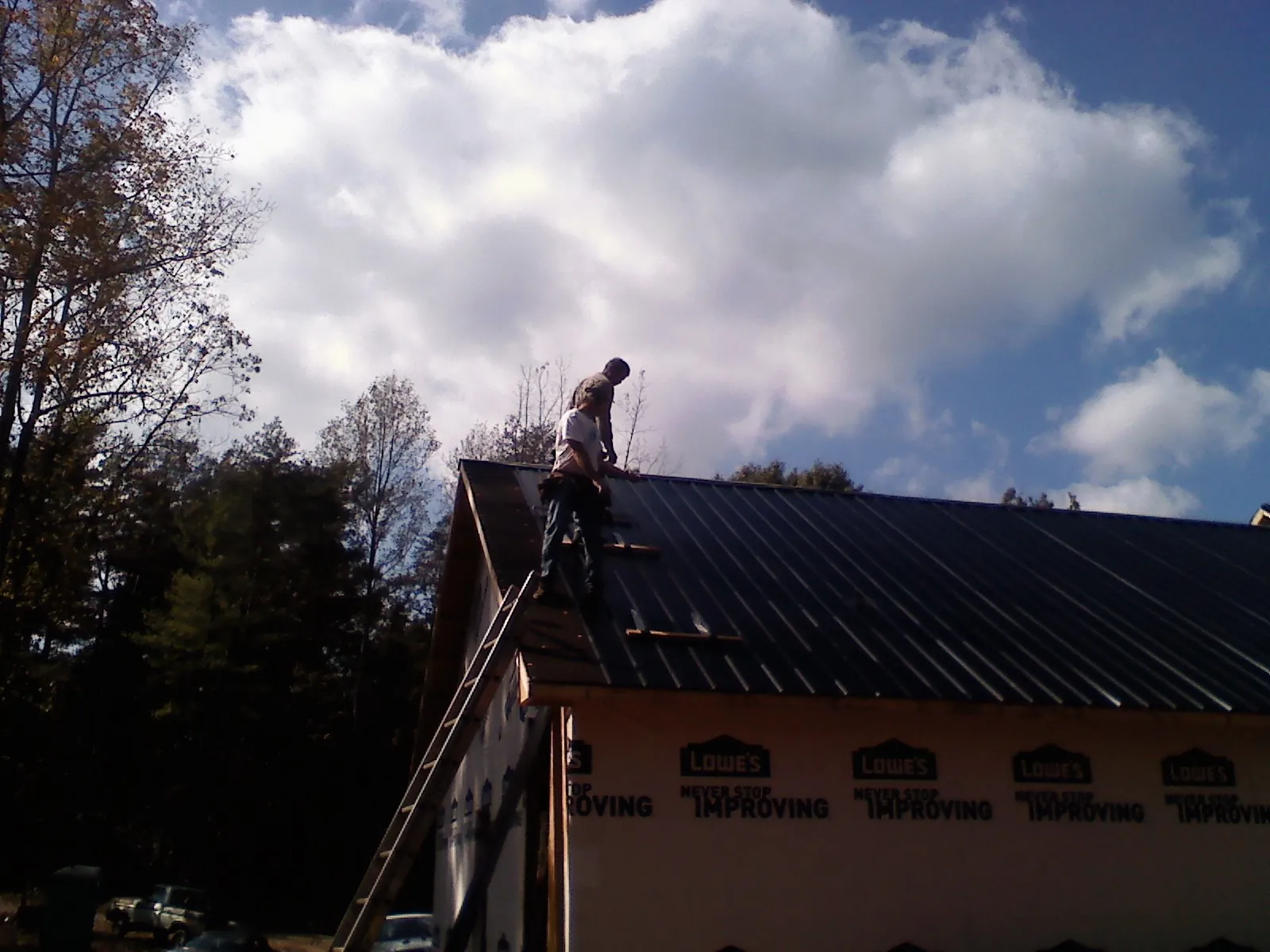 Roofer fastening dark metal panels high against a cloudy sky, from a Roof Inspection job in Beallsville